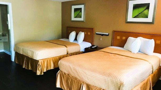 Una habitación de hotel con dos camas, paredes color crema y cuadros enmarcados.