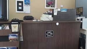 Un mostrador de recepción con un cartel que indica la hora de salida, una computadora y un cuadro en la pared.
