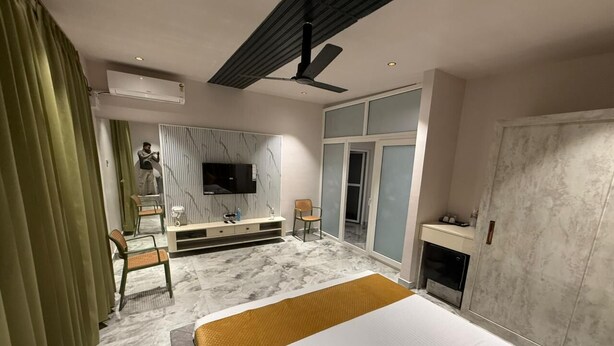 Habitación de hotel moderna con una cama grande, un televisor de pantalla plana, una zona de estar con sofá y sillones, una chimenea y un ventanal corredero.
