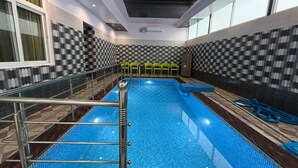 Una piscina interior con un diseño de pared a cuadros, una escalera de metal y una zona de estar con sillas.