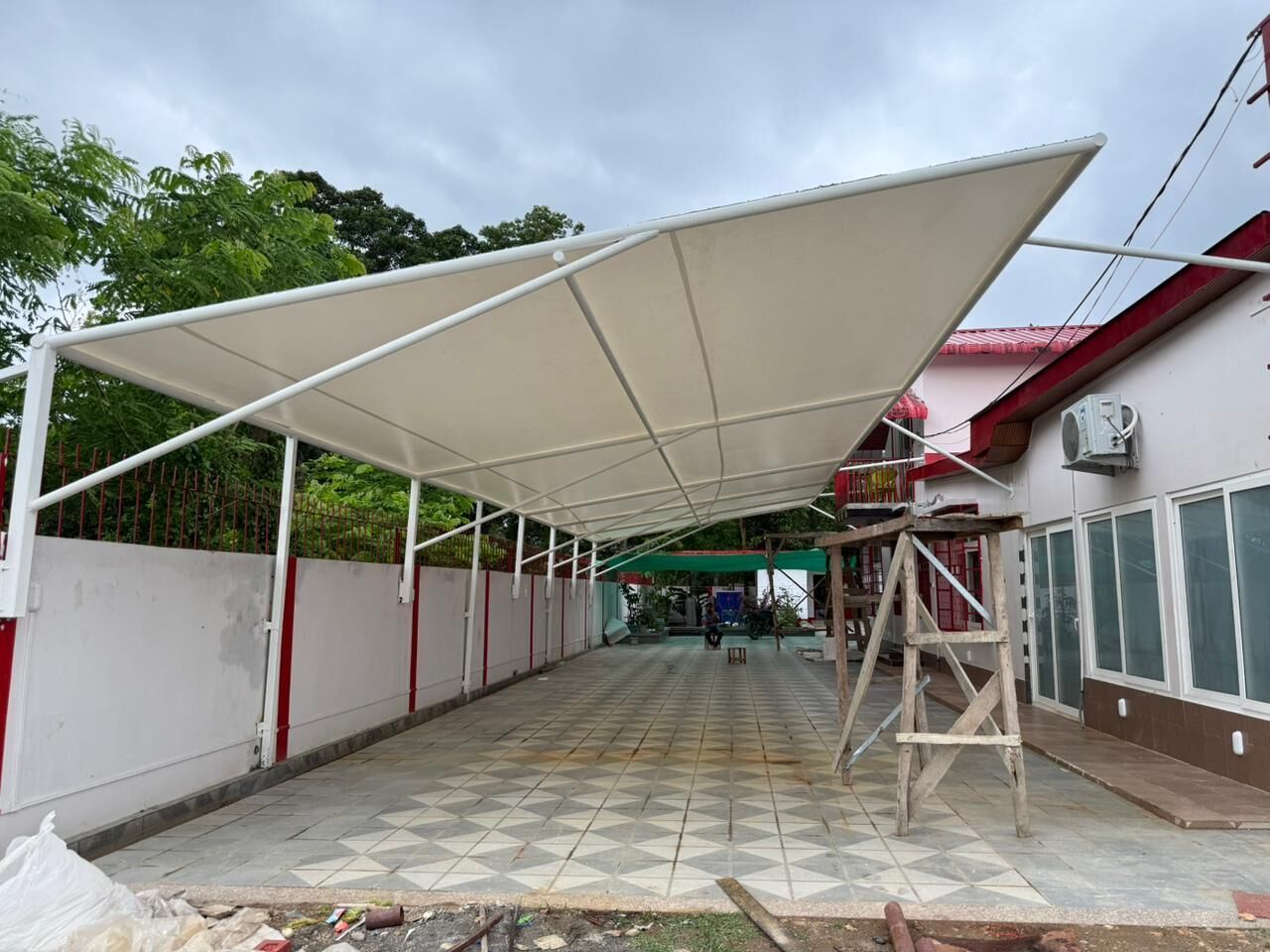Un espace extérieur abrité, doté d’un sol carrelé, d’un auvent blanc et d’une échelle en bois.