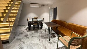 Una habitación con una escalera, una mesa de comedor con sillas, un sofá y un aire acondicionado instalado en el techo.