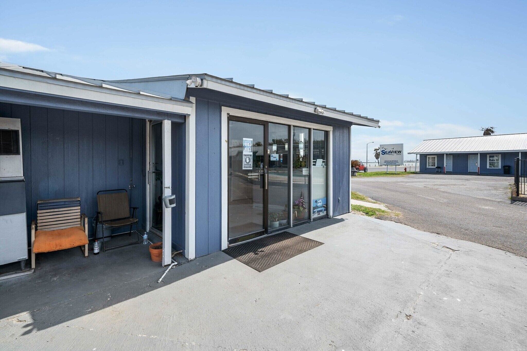 A building with a blue exterior, a glass door entrance, a bench outside, and a parking lot in the background.