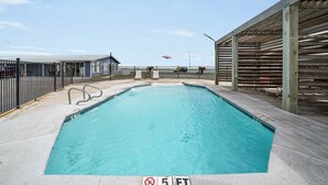 Ein rechteckiger Swimmingpool mit einem tiefenlimit-Schild von 5 Fuß, umzäunt, mit einem überdachten Bereich und Bänken.