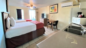 A hotel room with a bed, a desk, a chair, a sink, and a ceiling fan.