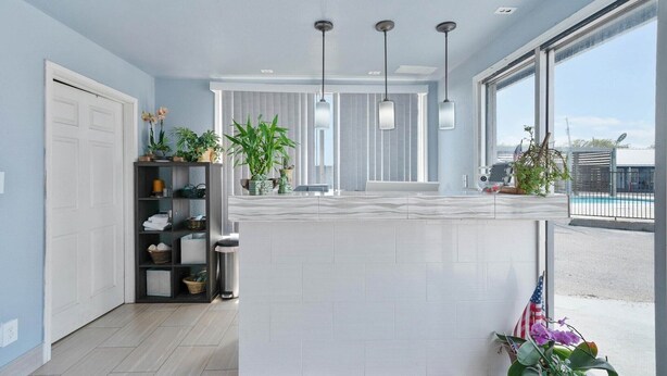 A modern kitchen with a white countertop, hanging pendant lights, and a view of the outside.