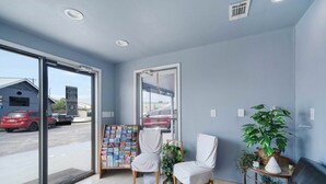 A reception area with a glass door, a seating area with chairs, a small table with a plant, and a bookshelf with magazines.