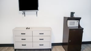 Une pièce avec une commode blanche, un téléviseur fixé au mur et un four à micro-ondes posé sur un meuble.