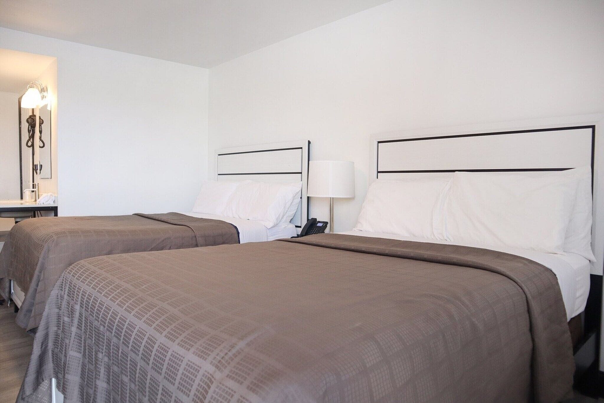 A hotel room with two beds, a bedside table with a lamp, and a mirror.