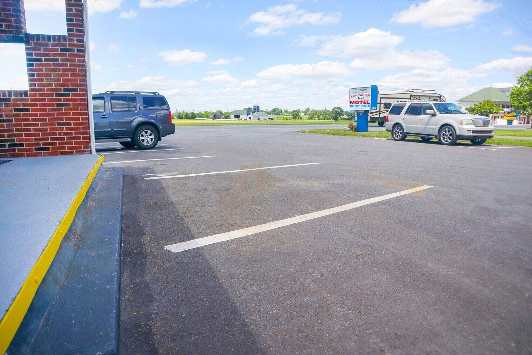 A parking lot with two cars, a brick building, and a sign for the Lancaster Motel.