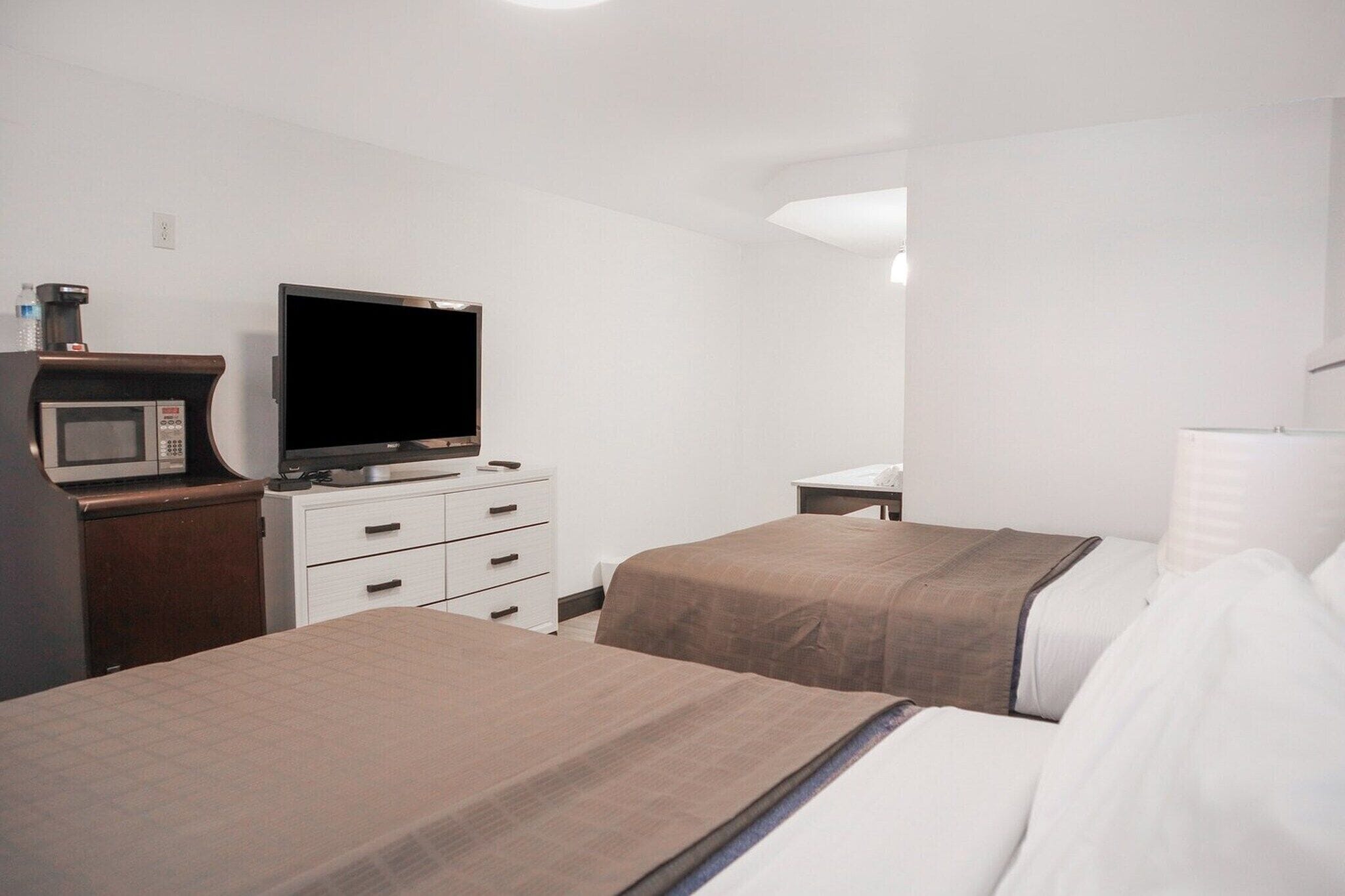 A hotel room with two beds, a TV, a microwave, and a small desk.