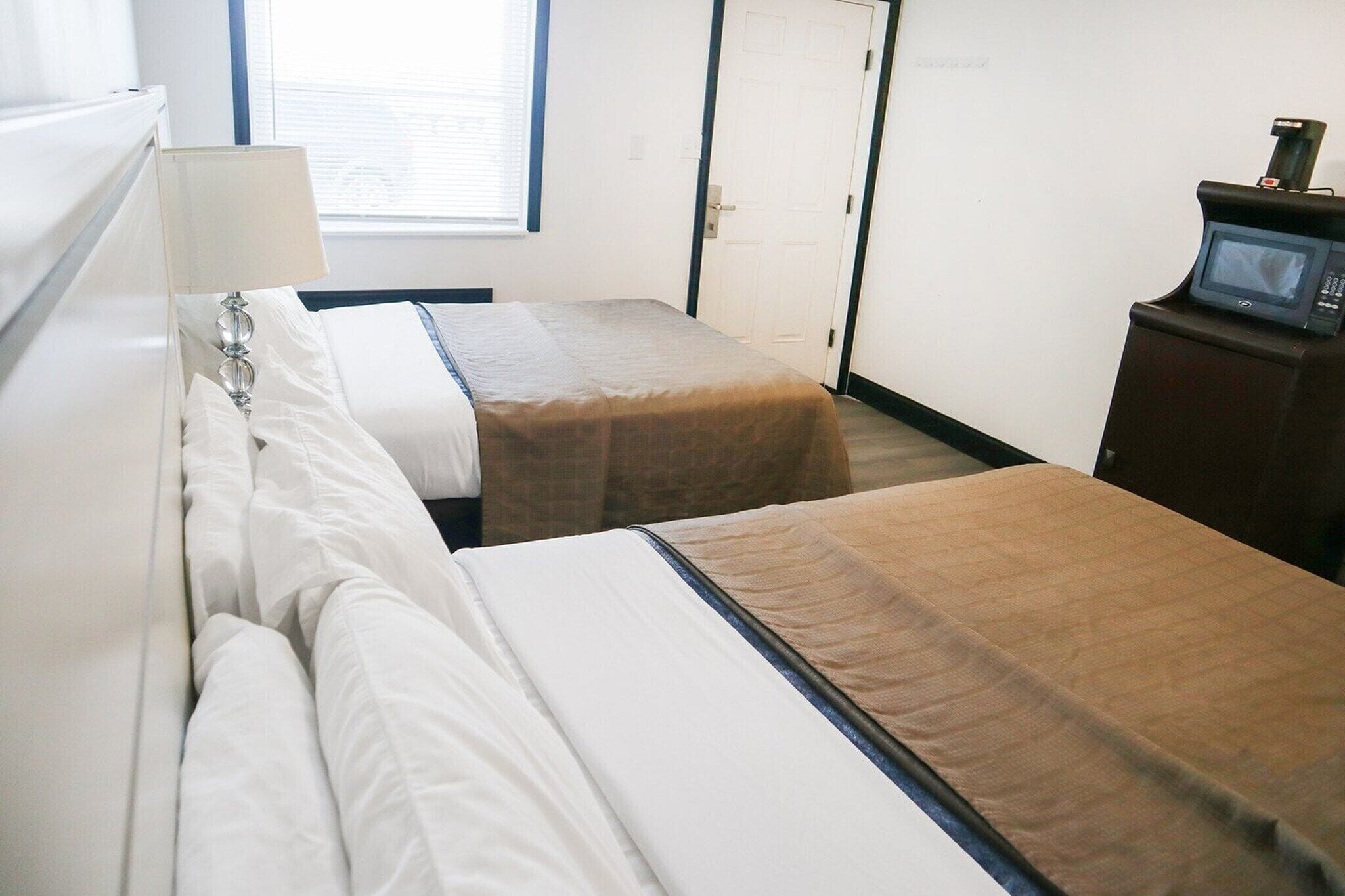 A hotel room with two beds, a bedside lamp, a microwave, and a door.