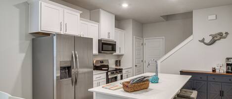 A modern kitchen with white cabinetry, stainless steel appliances, and a central island with bar stools.