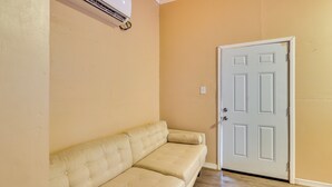 A beige sofa, a white door, and an air conditioning unit mounted on the wall. - Guest House Near Amphitheatre & Hard Rock Casino! (Tampa)