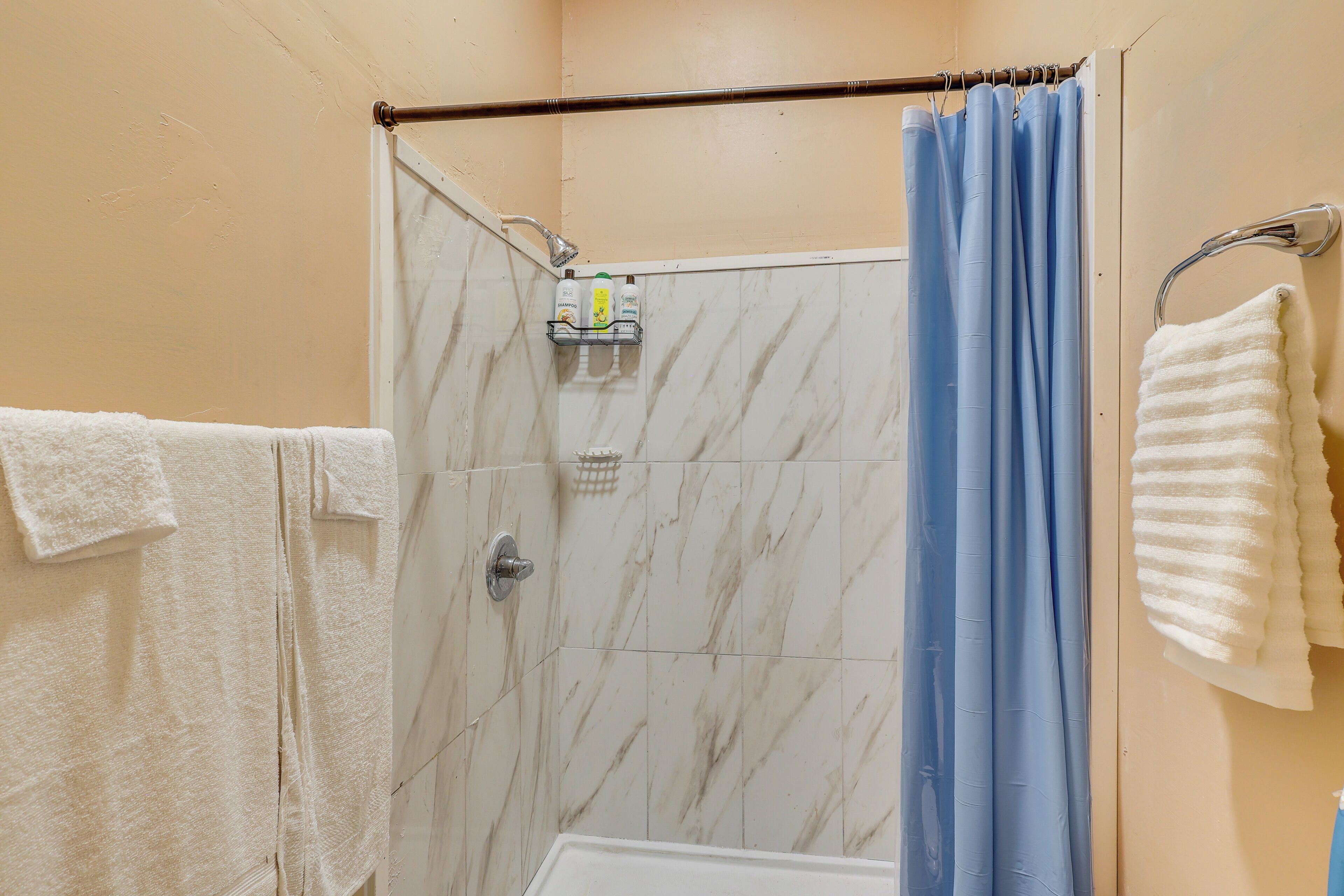 A shower area with a white bathtub, a blue shower curtain, and a towel rack with a white towel.