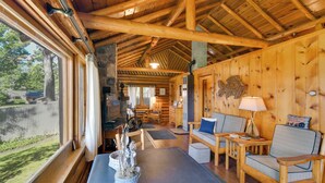 Eine Blockhütte mit Essbereich, einer Couch, einer Lampe und Blick ins Freie.