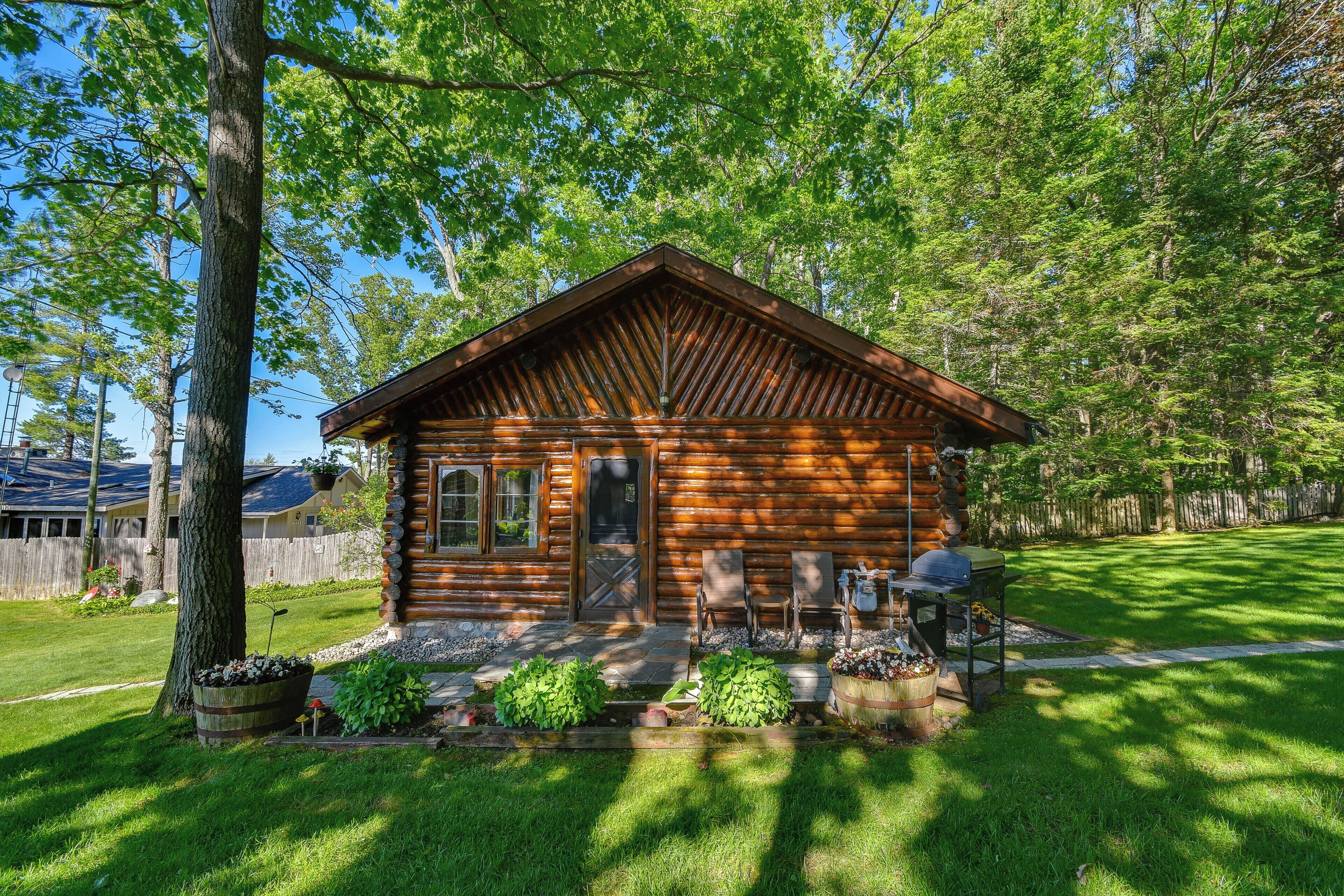 A log cabin with a porch, a grill, and a well-maintained lawn.