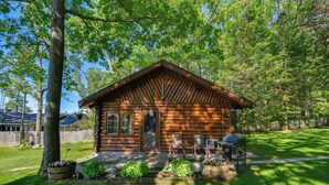 Eine Blockhütte mit Veranda, Grill und gepflegtem Rasen.