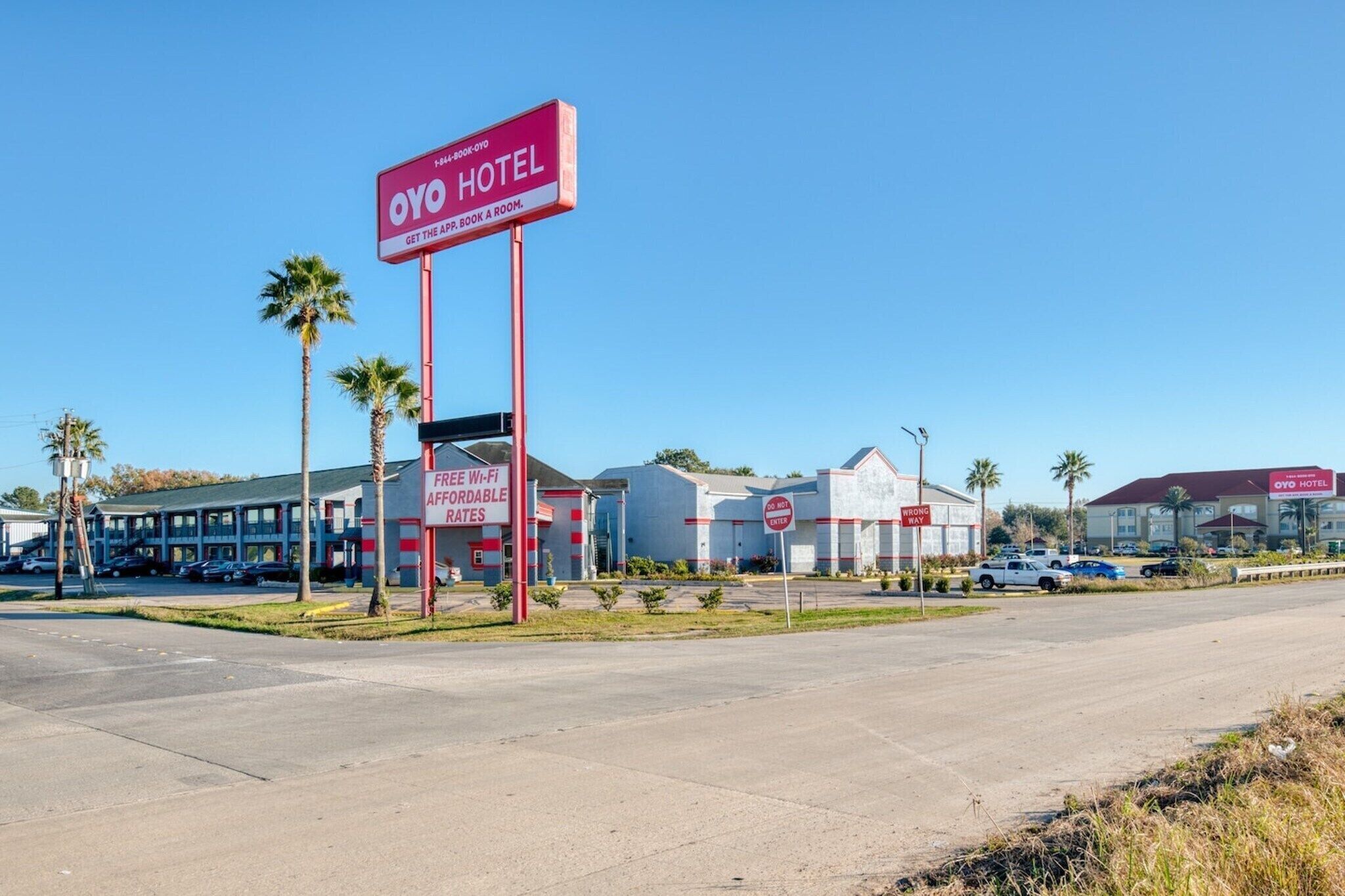 A hotel with a prominent sign, a parking lot, and a building with a red roof.