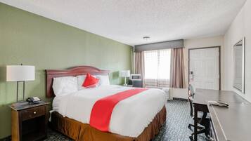 A hotel room with a bed, desk, chair, lamp, and a window with curtains.