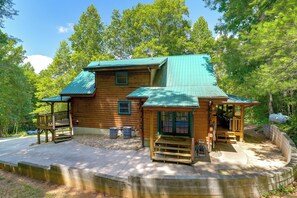 Eine Holzhütte mit grüner Dachdeckung, einer Veranda und einer kleinen Terrasse.