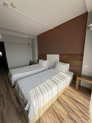 Habitación de hotel con dos camas, cabecero de madera, mesita de noche y velador.