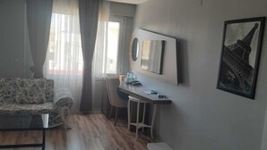 A modern living room with a sofa, a desk, and a chair. There is a window with curtains, a picture of the Eiffel Tower, and a bench. - Yalim Garden Park Otel (Sivasli)