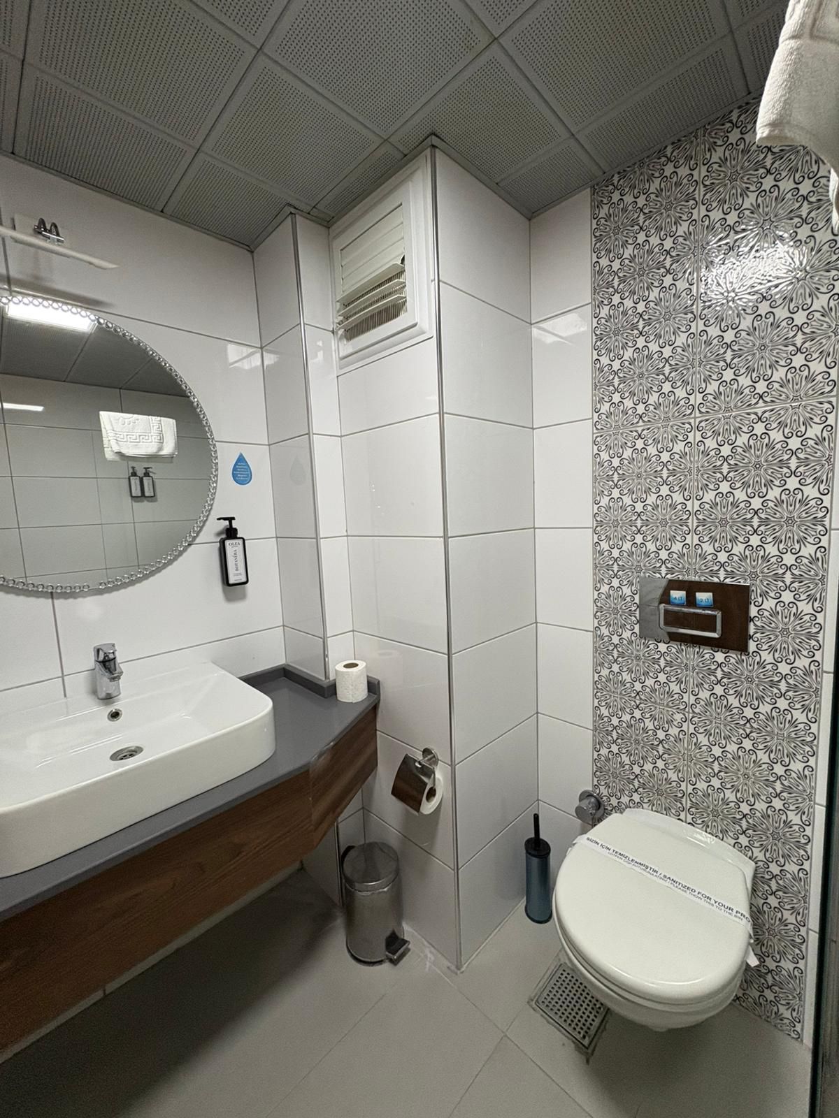 Un baño con lavamanos blanco, espejo, inodoro y azulejos con diseño.