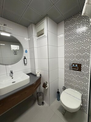 Un baño con lavamanos blanco, espejo, inodoro y azulejos con diseño.