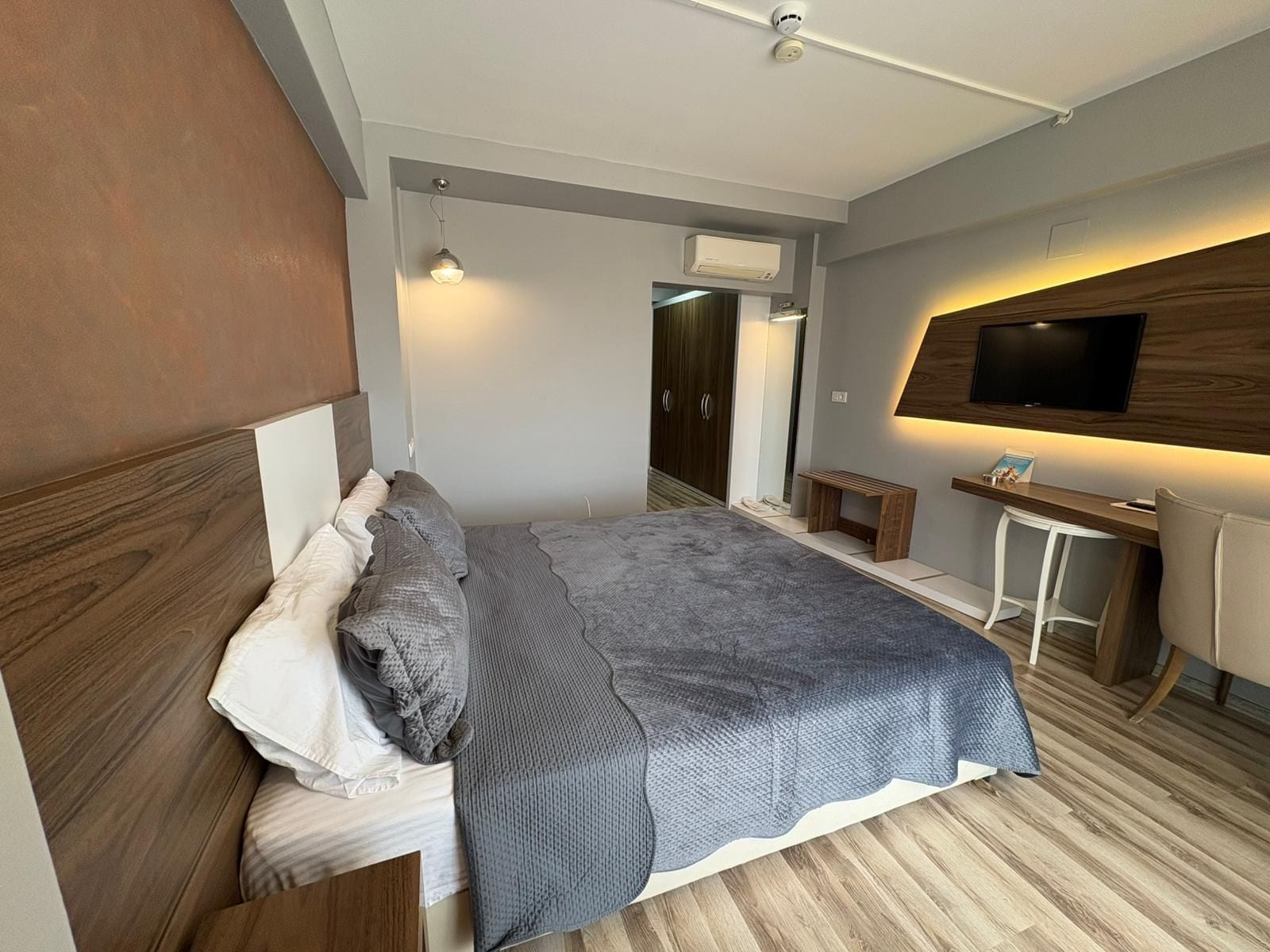 Un dormitorio moderno con cama, mesita de noche y televisor montado en la pared.