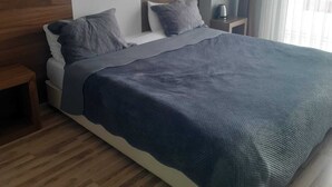 A modern hotel room with a large bed, wooden flooring, a nightstand, and a window with curtains. - Yalim Garden Park Otel (Sivasli)