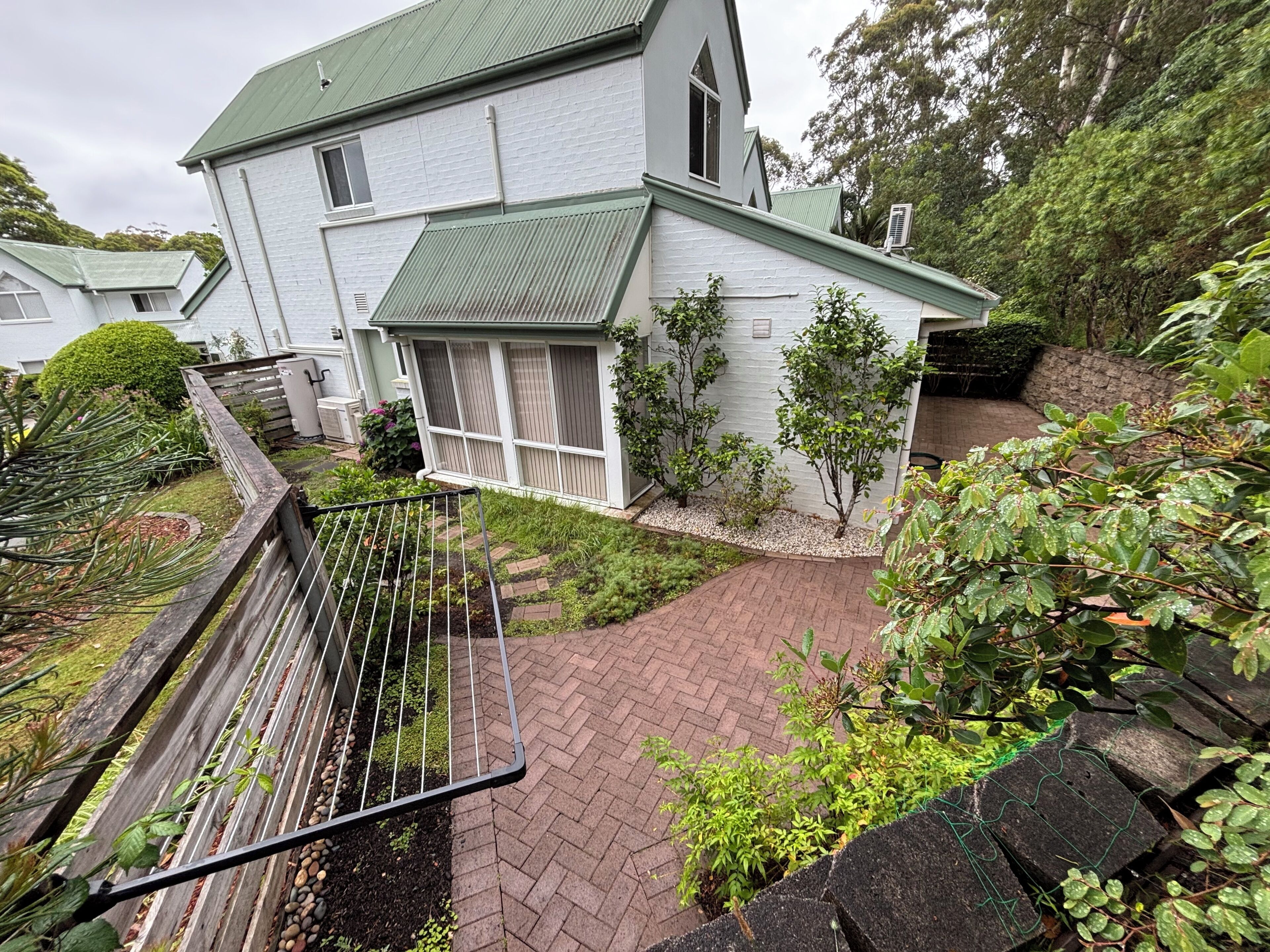 A two-story house with a green roof, a brick pathway, and a metal railing.