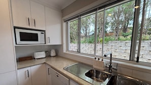 A kitchen with white cabinets, a microwave, a toaster, and a sink. - Mollymook Beach Townhouse on the Hilltop Golf Course and minutes to the beach (Mollymook Beach)