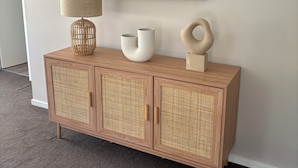 A wooden cabinet with woven doors, a lamp, and decorative items on a wall. - Mollymook Beach Townhouse on the Hilltop Golf Course and minutes to the beach (Mollymook Beach)