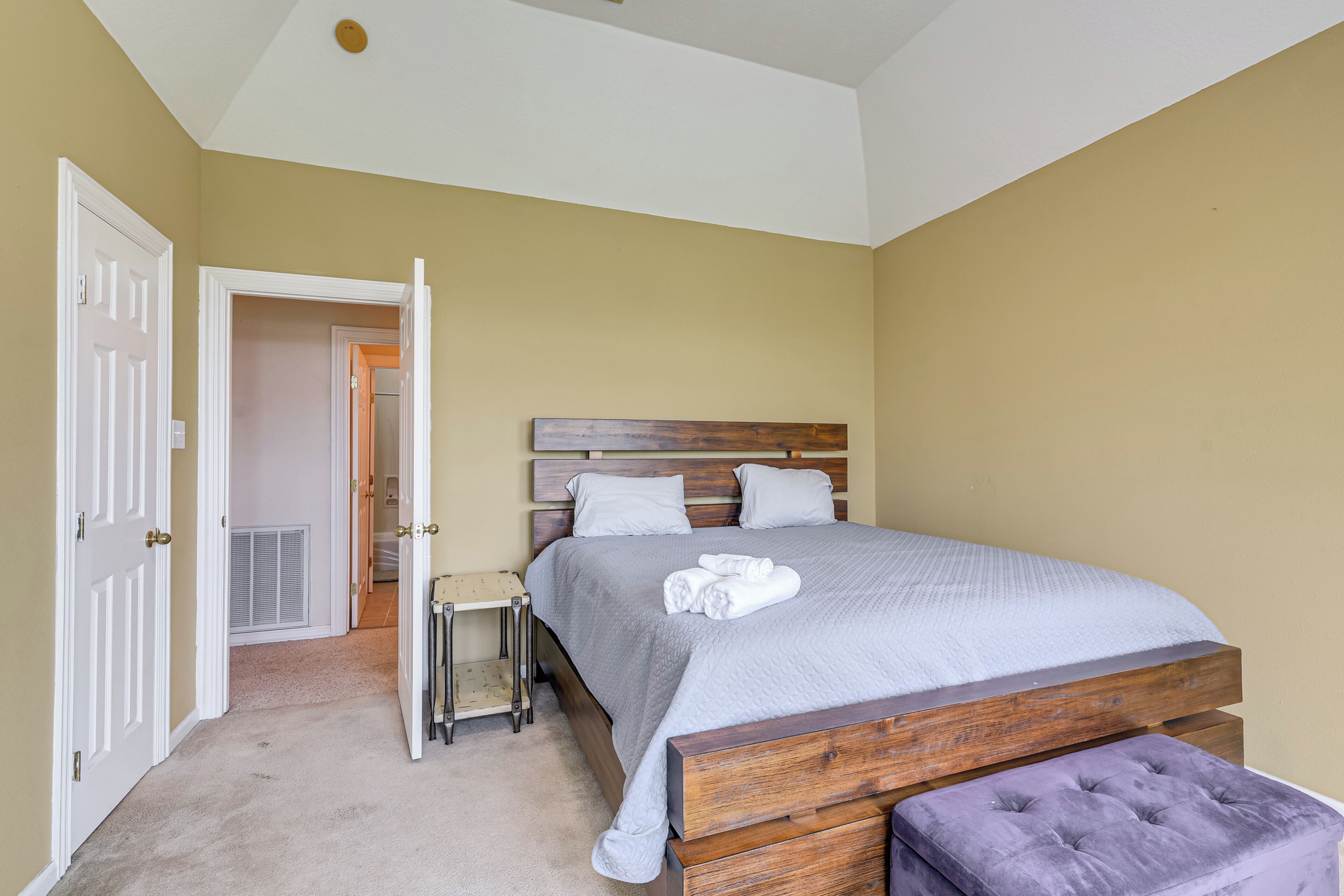 A bedroom with a bed, a bench, and a door leading to another room.