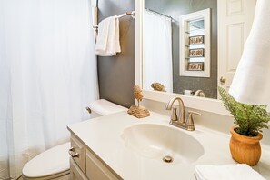 Un bagno con lavandino, specchio, porta asciugamani e una pianta in vaso.