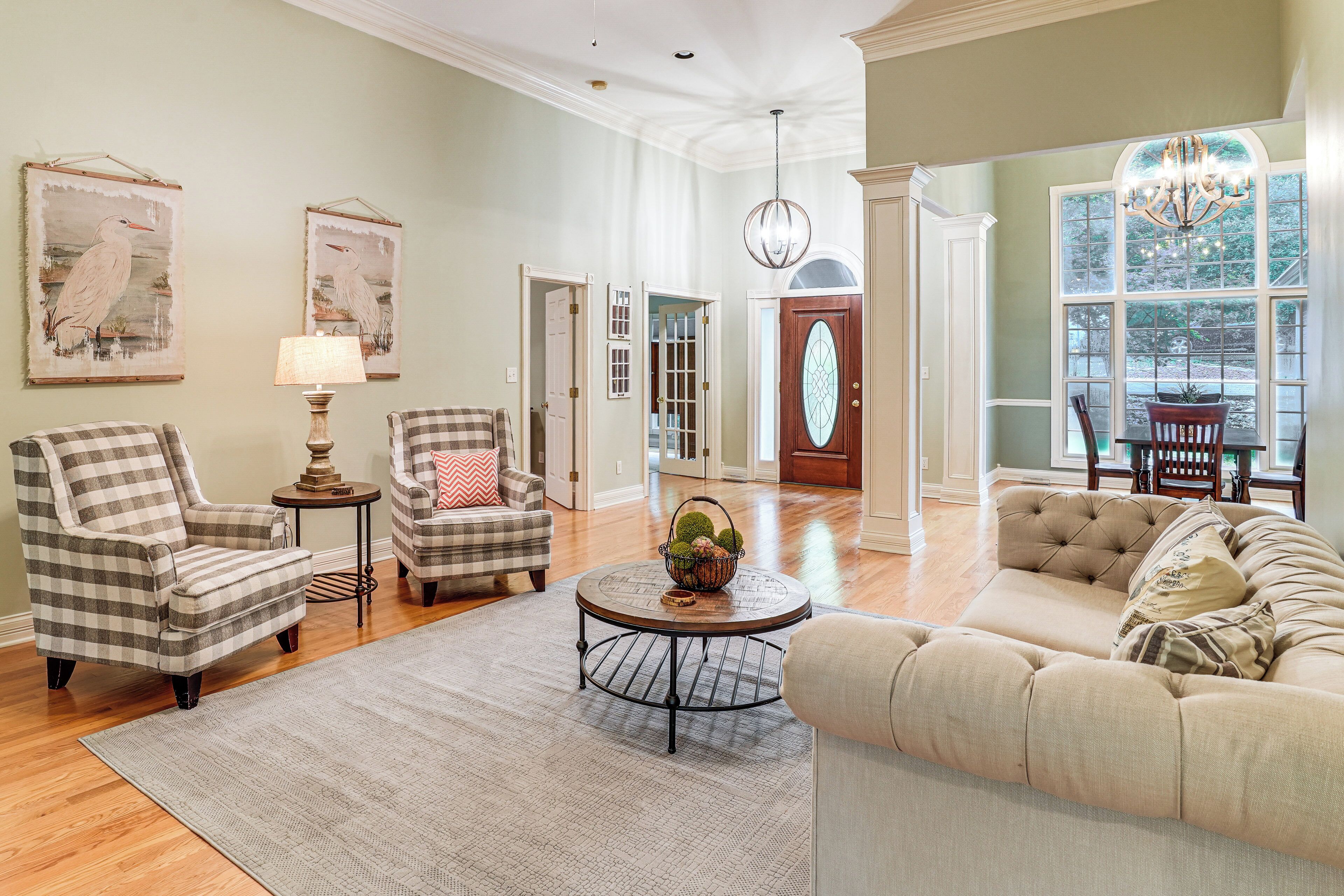 A living room with a checkered armchair, a round coffee table with a basket, a beige sofa, and a chandelier.