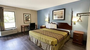 A hotel room with a bed, desk, chair, bedside tables, and a window. - King Bed Non-Smoking (Ridgeway, SC)
