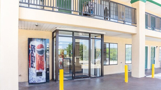 Ein Gebäudeeingang mit Glastür, einer Pepsi-Getränkeautomaten und einem Balkon.
