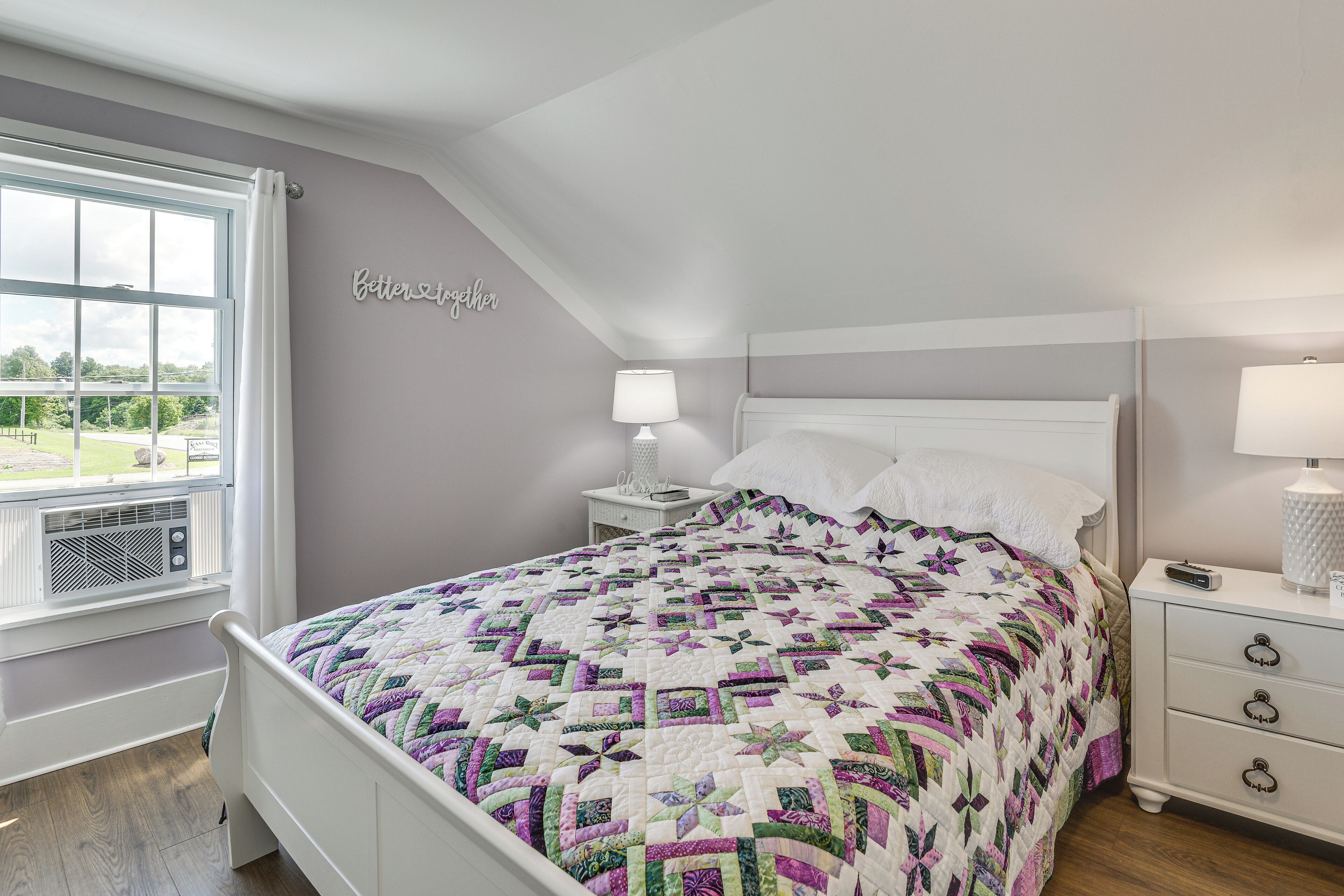 Een slaapkamer met een bed, nachtkastjes, een raam en een bord aan de muur.
