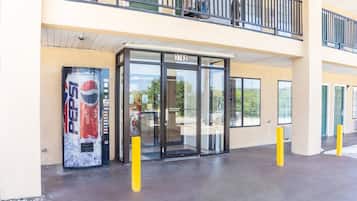 A building entrance with a glass door, a Pepsi vending machine, and a yellow bollard.