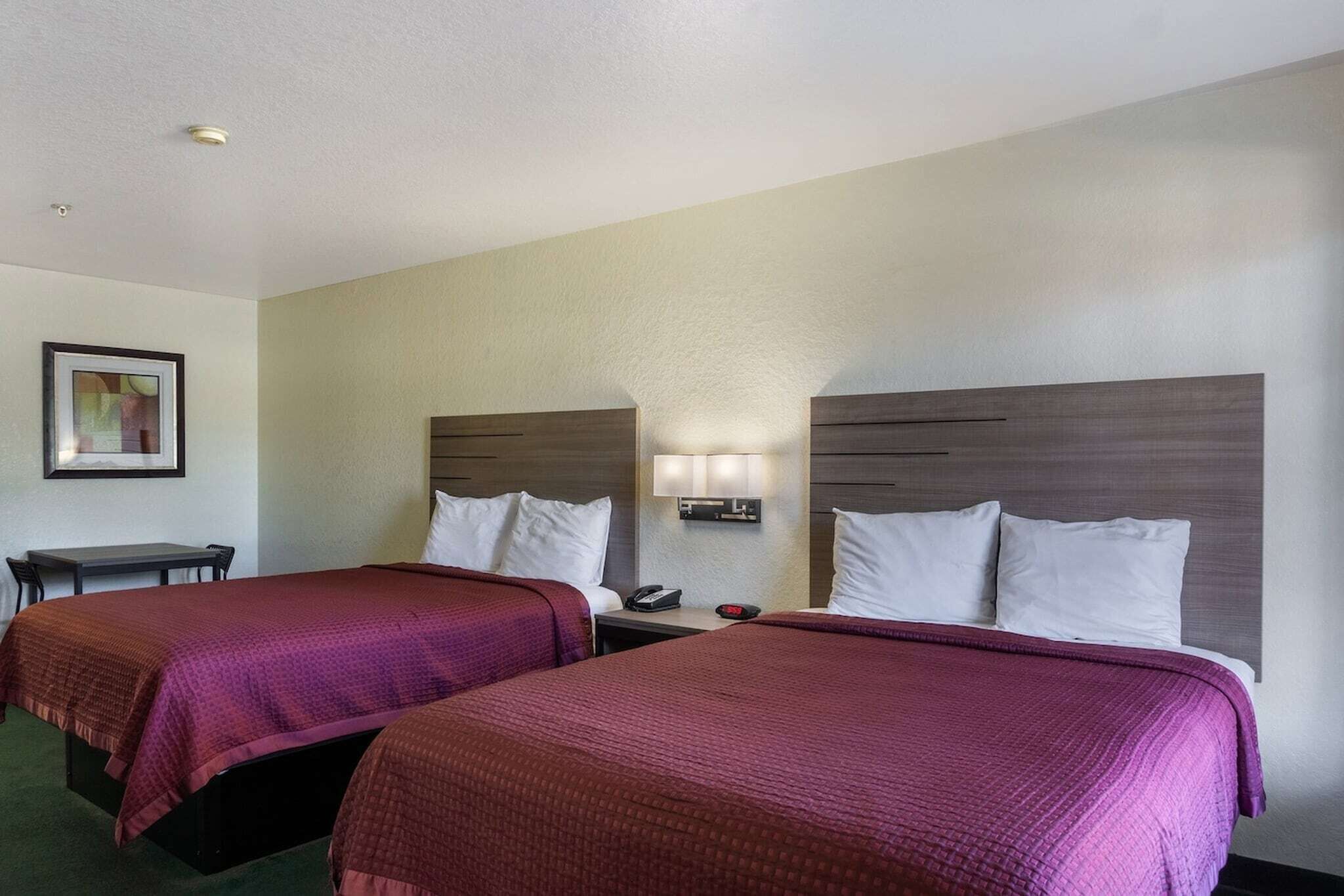 A hotel room with two beds, a desk, and a nightstand with a lamp.