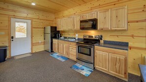Cocina con paneles de madera, refrigerador, microondas, estufa y gabinetes.