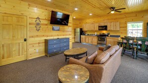 Un interior de madera con sofá, mesa de centro, televisor, zona de cocina y mesa de comedor.
