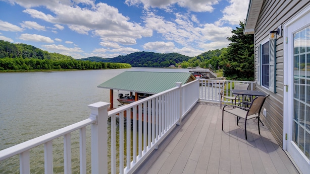 Une terrasse avec vue sur un lac et des montagnes, une table et des chaises, et un bâtiment doté d’un toit végétalisé.