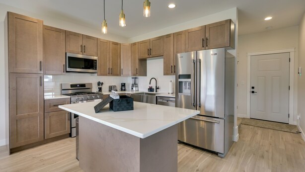 Una cocina moderna con armarios de madera, electrodomésticos de acero inoxidable e iluminación colgante.