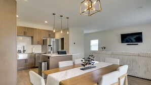Una cocina moderna con electrodomésticos de acero inoxidable, un comedor con mesa y sillas de madera, y una sala de estar con sofá y televisor montado en la pared.
