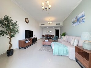 A modern living room with a flat-screen TV, a wooden entertainment unit, a sofa, a coffee table, and a dining area in the background. - Luxury 3BR  Sea & Skyline View  Noor Mosque view (Sharjah)