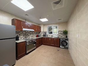 A kitchen with wooden cabinets, a stainless steel refrigerator, a stove, a dishwasher, and a window. - Luxury 3BR  Sea & Skyline View  Noor Mosque view (Sharjah)