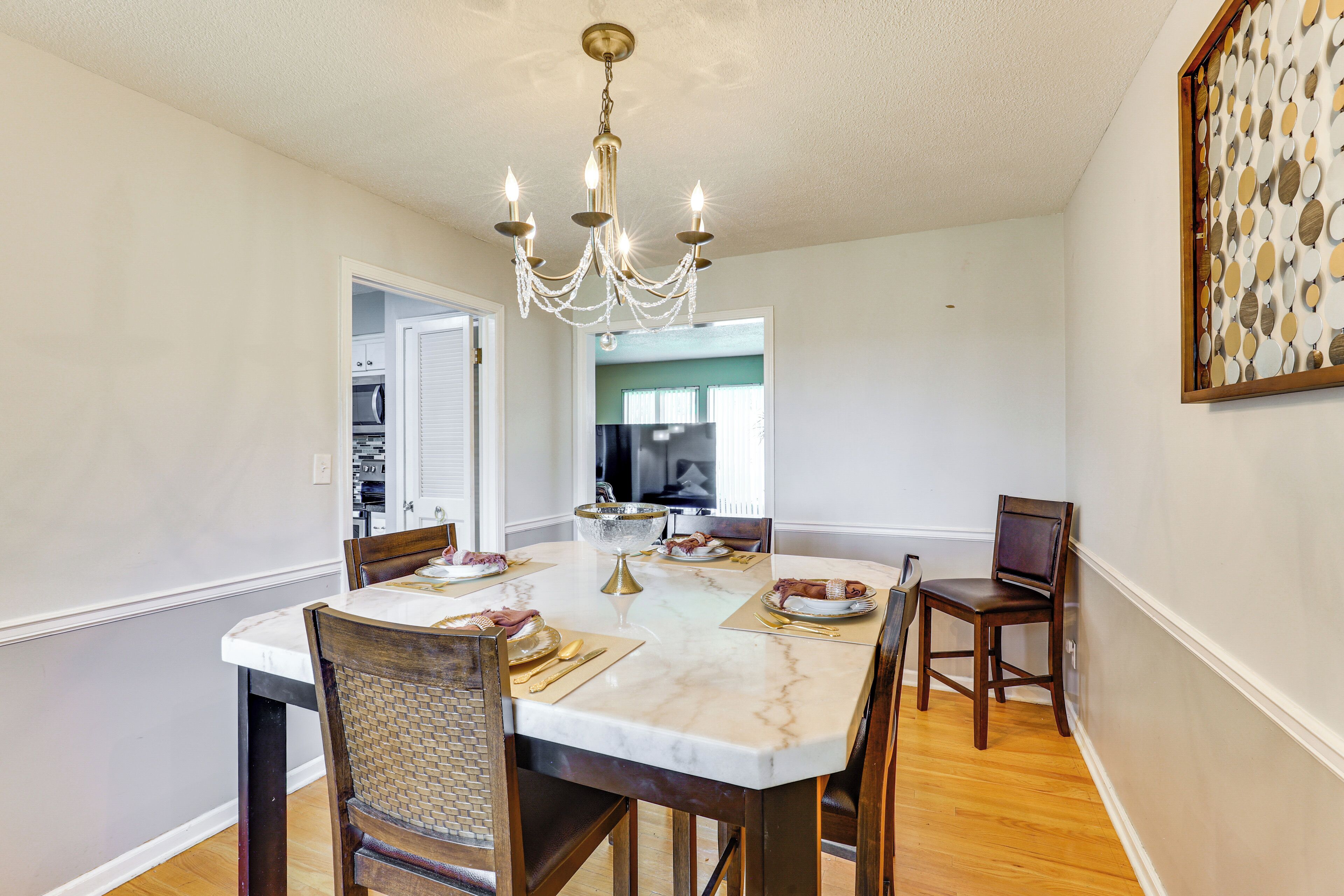 A dining area with a marble table, wooden chairs, a chandelier, and a kitchen in the background.